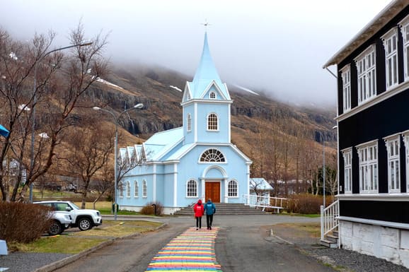 Zwei Kreuzfahrtgäste gehen zur Seyðisfjarðarkirkja Kirche, die bekannt als die Blaue Kirche, im malerischen Ort Seyðisfjörður im Osten Island, ist.